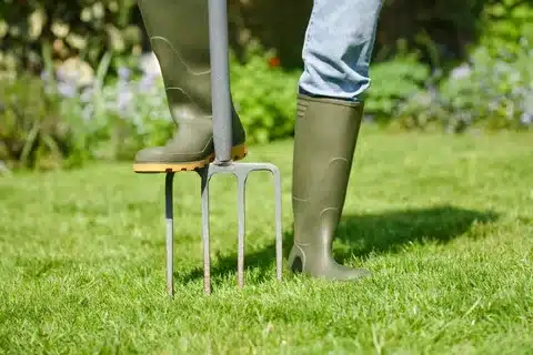 A person in green boots standing on a small fork while providing Lawn Aeration Services, promoting a healthy lawn.