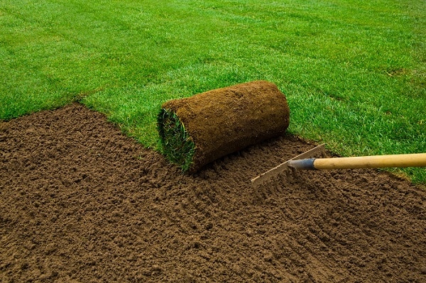 A person spreading soil with a rake, preparing the ground for gardening or landscaping.